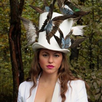 Portrait of Jerike Broussard in a white hat with feathers attached in the shape of butterflies