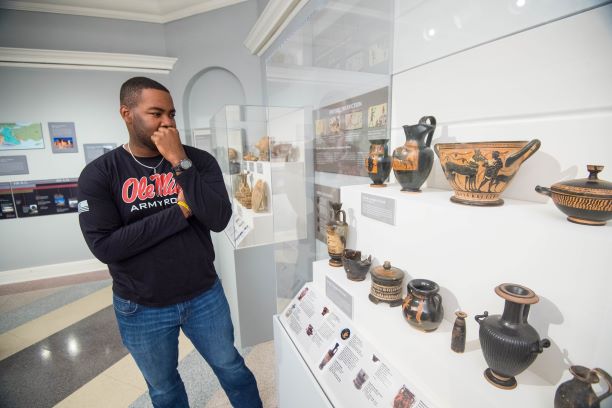An African American male student is viewing the Robinson Collection of ancient Greek pottery at the UM Museum