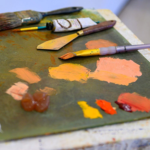 A paint pallette with dabs of orange and red paint, brushes, and other tools.
