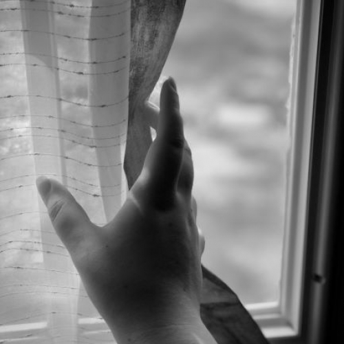 A photo of a hand holding a curtain at a window.