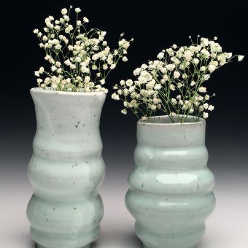 Two light green vases holding white flowers